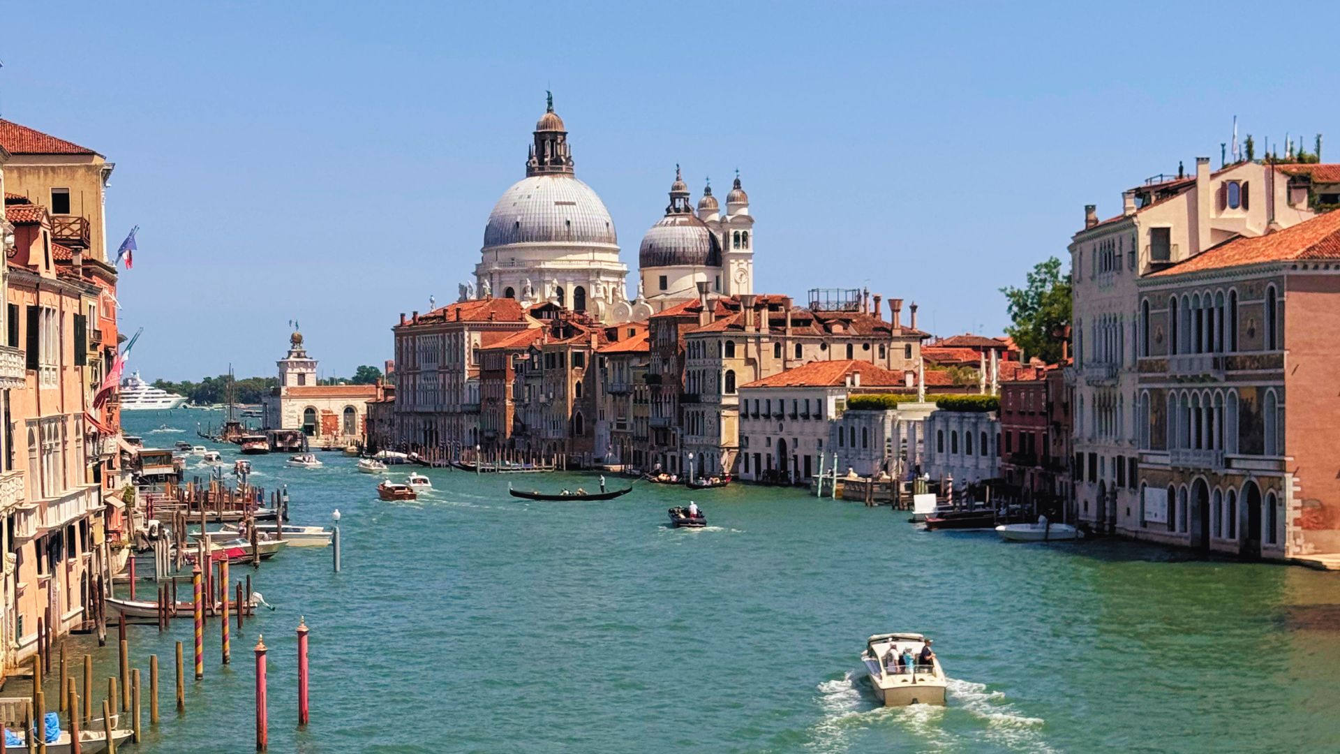 Il Canal Grande di Venezia visto dal Ponte dell'Accademia, con la cupola della Basilica di Santa Maria della Salute sullo sfondo, gondole e imbarcazioni sull'acqua.